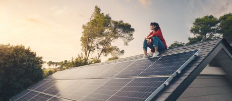 Frau sitzt auf einem Dach mit Photovoltaik-Anlage